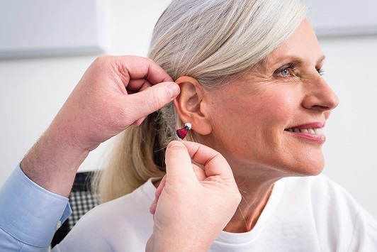 Seniorin bekommt ein modernes Hörgerät angepasst, Hörakustik und Hörhilfe Beratung.